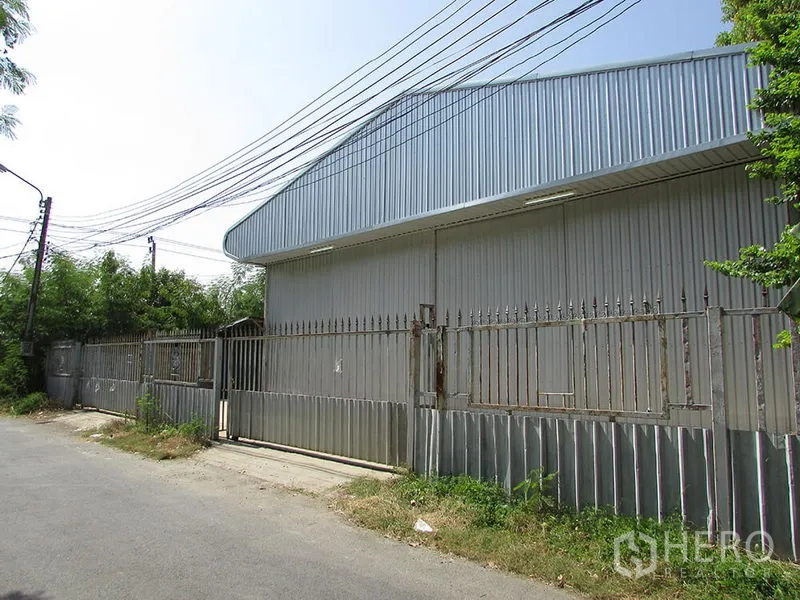 货栈 出租在Bang Khen, Bangkok - 邦肯安静小路旁的镀锌金属仓库外观，带围栏与大型滑动门。