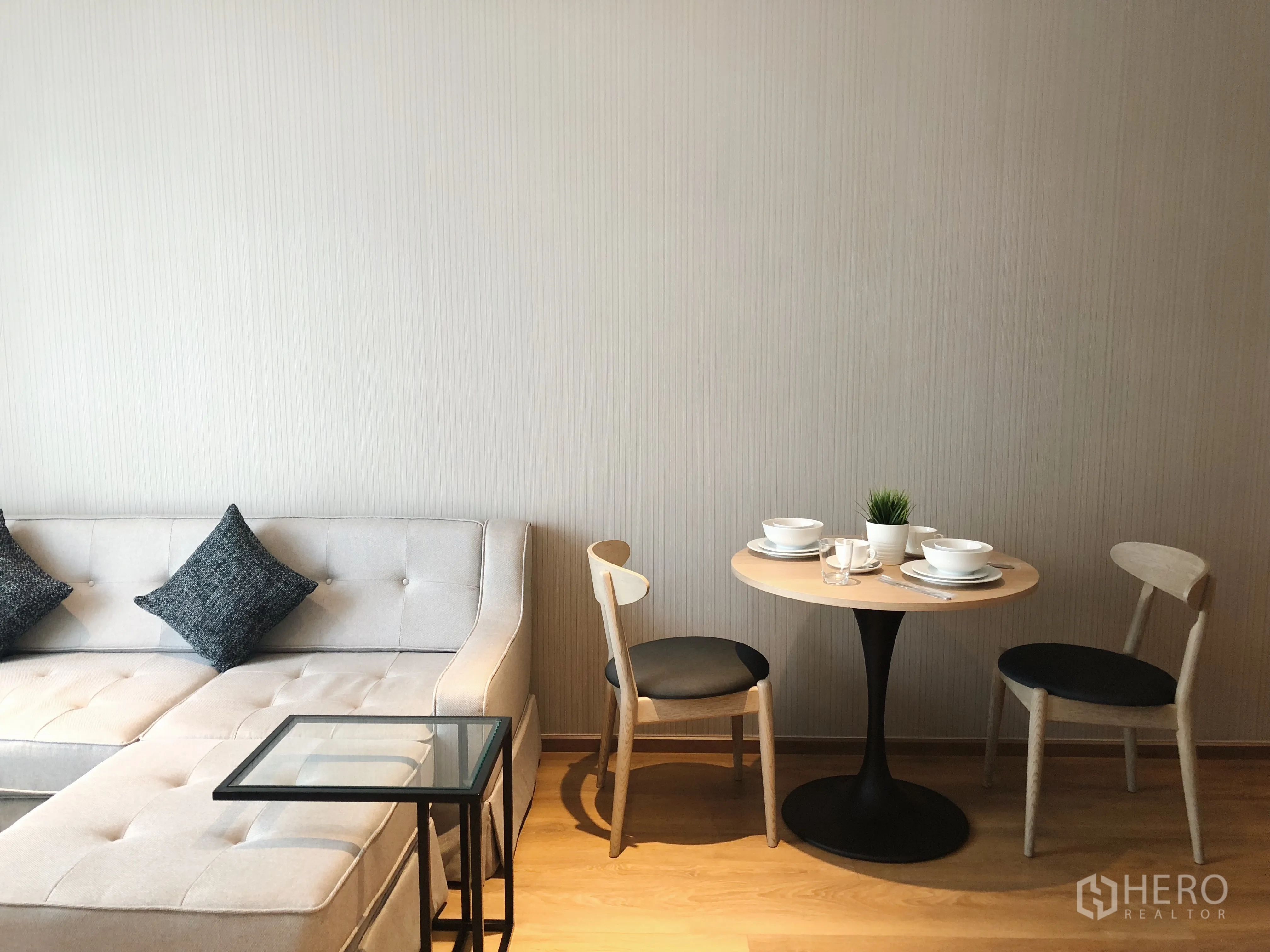 Condominium for rent in Khlong Toei, Bangkok - Compact dining nook with round table and two chairs beside sectional sofa in a bright lounge.
