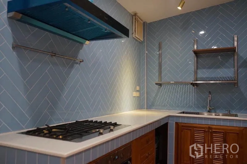 Detached House for rent in Wang Thonglang, Bangkok - U-shaped kitchen with blue herringbone tiles, gas hob, range hood and open shelves.