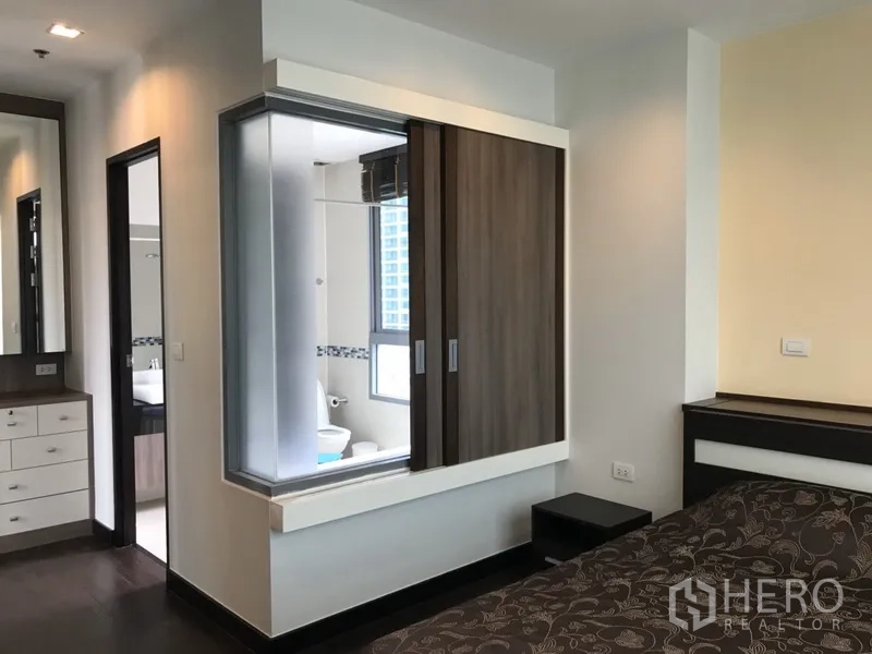 Condominium for rent in Ratchathewi, Bangkok - Bedroom corridor with built-in wardrobe, dressing area and a glass partition looking into the ensuite bathroom.