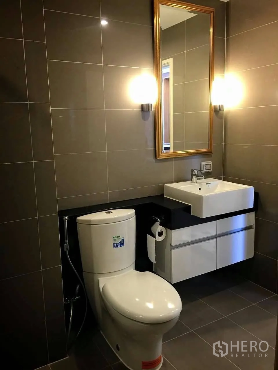 Condominium for sale in Huai Khwang, Bangkok - Contemporary bathroom with grey tiles, gold-framed mirror, floating vanity and toilet.