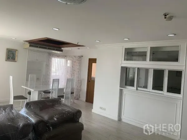 Condominium for rent in Watthana, Bangkok - Dining area with white table and high-back chairs, built-in shelving, recessed lighting and sliding glass door with curtains.