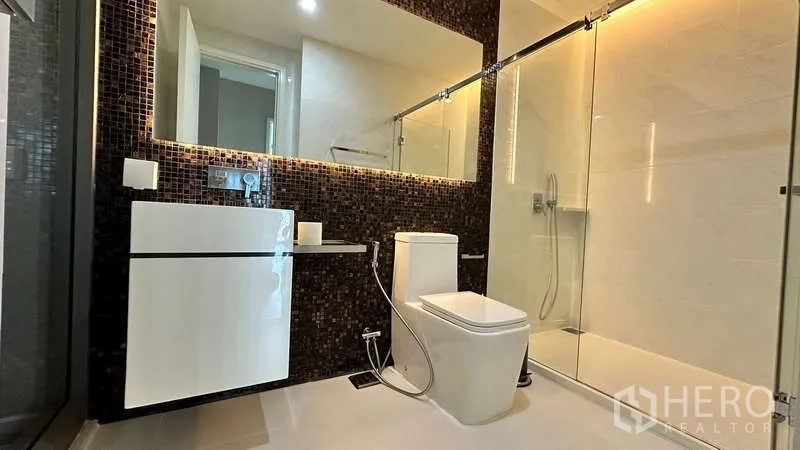 Condominium for rent - Sleek bathroom with mosaic accent wall, illuminated mirror, floating vanity, and glass shower.