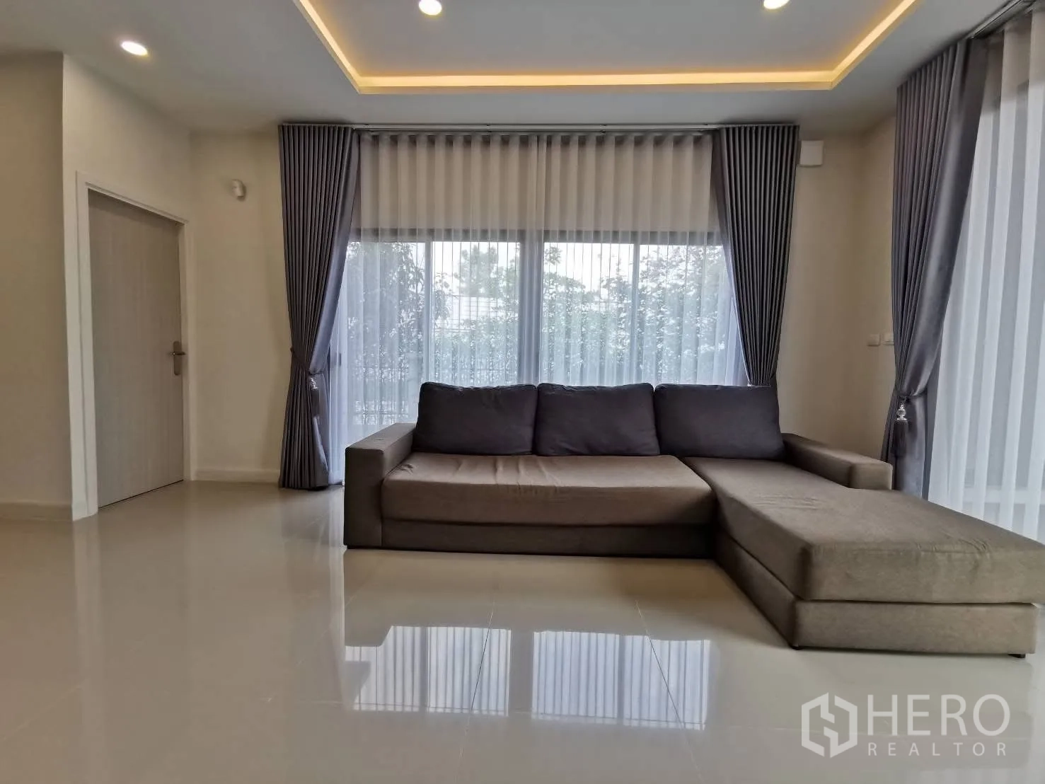 Detached House for rent in Bang Phli, Samut Prakan - Cozy lounge with sectional sofa, cove lighting, and floor-to-ceiling curtains.