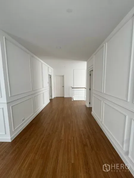 Detached House for rent or sale in Bang Bo, Samut Prakan - Upstairs hallway with wood flooring and white wall paneling leading to bedrooms.