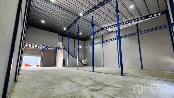คลังสินค้า ให้เช่าในKrathum Baen, Samut Sakhon - ภายในโกดังเพดานสูง เสาเหล็กสีน้ำเงิน พื้นคอนกรีตขัดมัน และประตูม้วนใหญ่ติดบันไดขึ้นออฟฟิศ