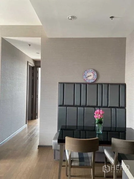 Condominium for sale in Bang Rak, Bangkok - Dining nook with padded bench seating, wall clock and black glass table with flowers.