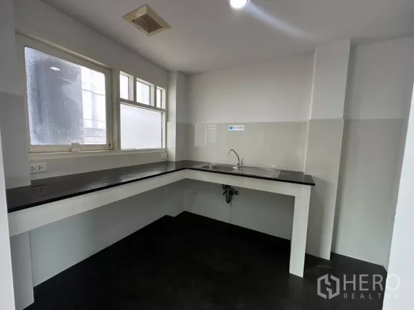 办公空间 出租在Watthana, Bangkok - 茶水间，L形黑色台面与不锈钢水槽，转角窗带来自然采光。