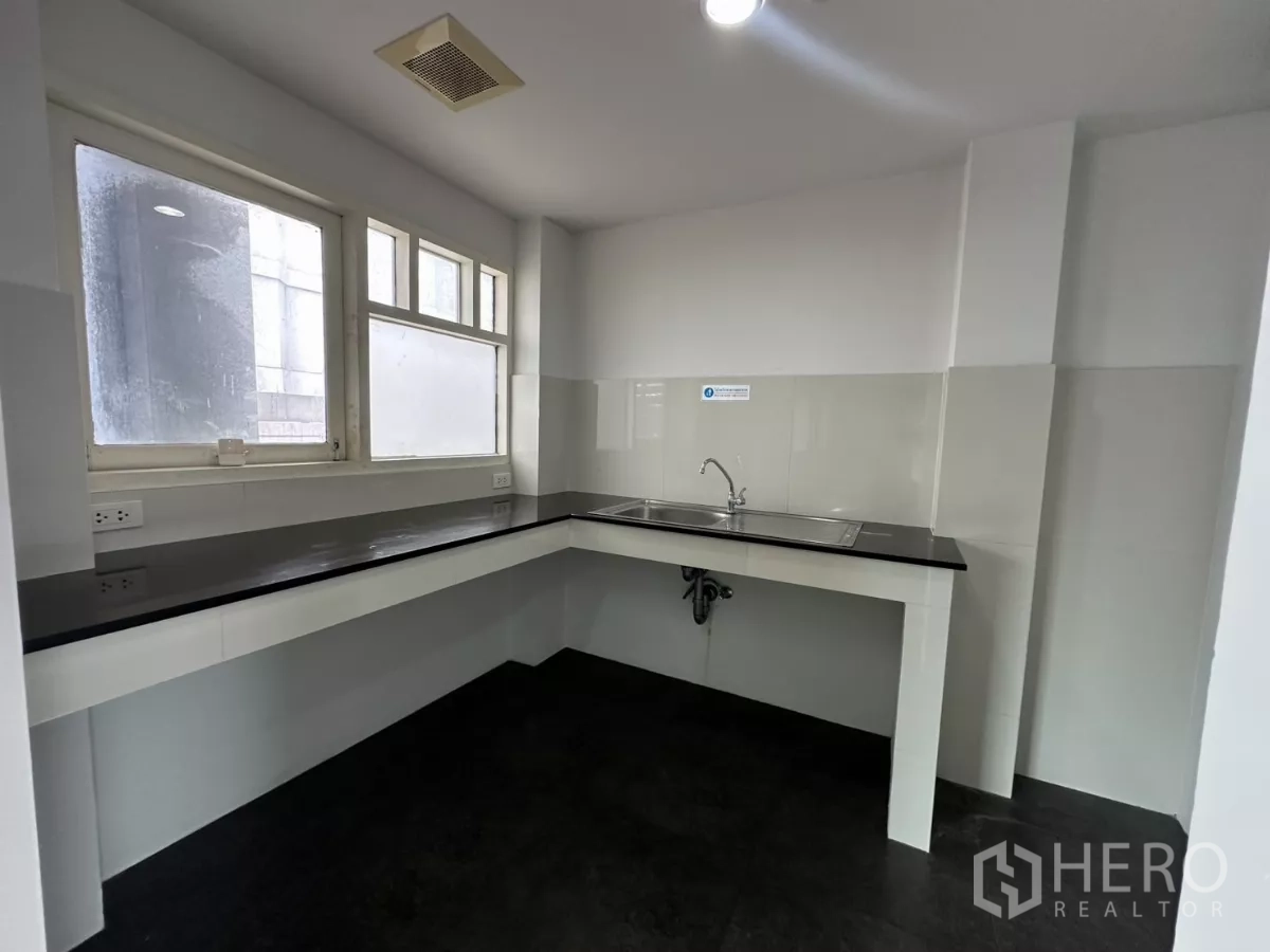 办公空间 出租在Watthana, Bangkok - 茶水间，L形黑色台面与不锈钢水槽，转角窗带来自然采光。