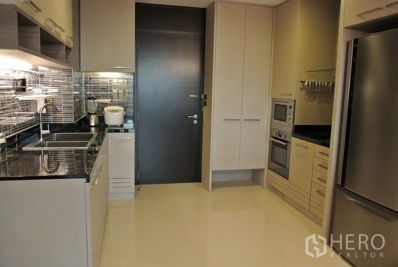 Condominium for rent or sale in Watthana, Bangkok - Modern separated kitchen with glossy tile backsplash, stone countertops, built-in oven and microwave, ample cabinetry, and a stainless refrigerator.