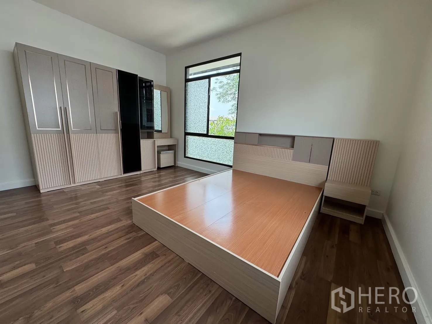 Detached House for rent in Prawet, Bangkok - Bedroom with platform bed and full wardrobe wall beside a large window.