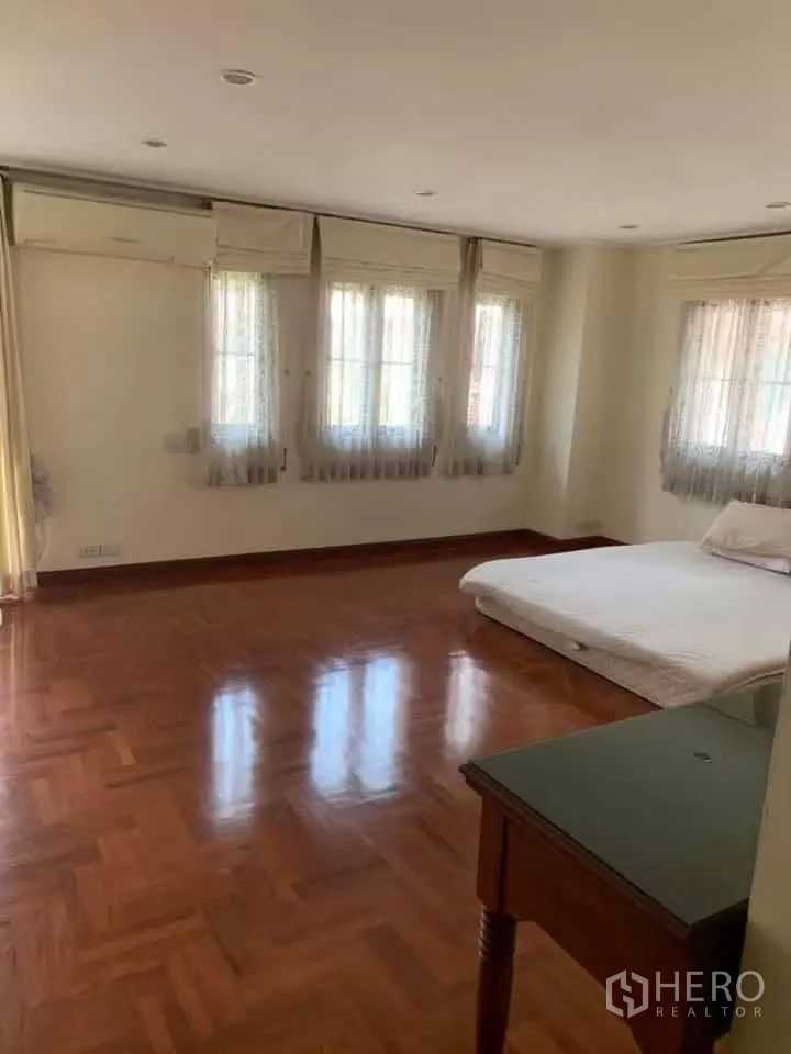 Townhouse for rent in Watthana, Bangkok - Large bedroom with multiple windows, wood floors, and a low platform bed.