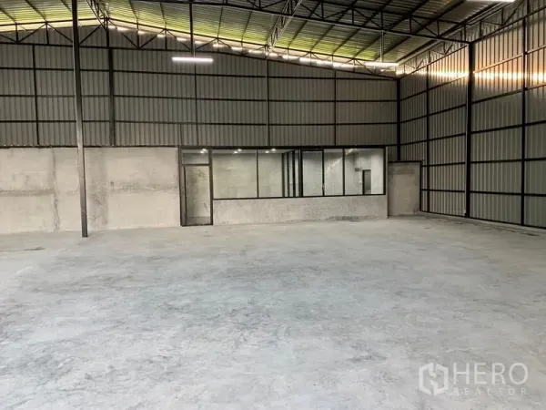 货栈 出租在Khan Na Yao, Bangkok - 仓库内部，高挑钢结构屋顶与混凝土地面，背墙设玻璃办公室和照明。