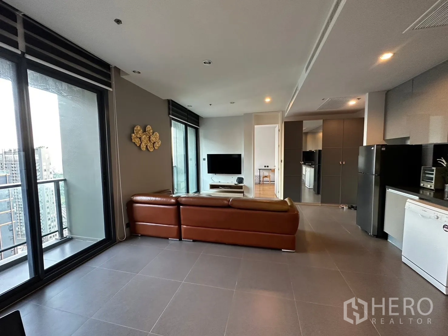 คอนโด for rent or sale in Chatuchak, Bangkok - ห้องนั่งเล่นโอเพ่นแพลน โซฟาหนังตัวแอล ทีวี และทางออกสู่ระเบียง