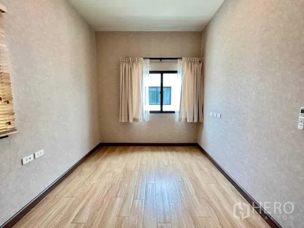 Detached House for rent in Khlong Sam Wa, Bangkok - Bright empty bedroom with wood-look flooring, beige walls and a curtained window
