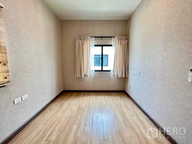 Detached House for rent in Khlong Sam Wa, Bangkok - Bright empty bedroom with wood-look flooring, beige walls and a curtained window