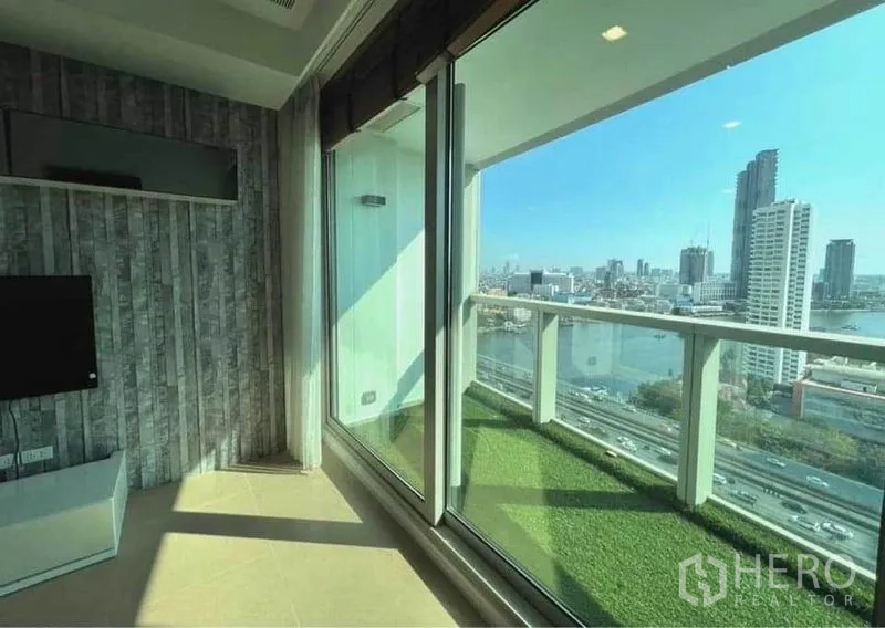 คอนโด ให้เช่าในKhlong San, Bangkok - พื้นที่นั่งเล่นมีประตูกระจกบานเลื่อนเต็มผนัง เปิดสู่ระเบียงหญ้าเทียมวิวแม่น้ำเจ้าพระยาและสกายไลน์