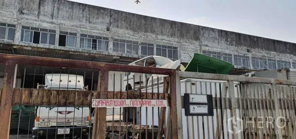 ที่ดิน ขายในLat Krabang, Bangkok - ประตูรั้วโลหะทางเข้า มีรถบรรทุกและอาคารโรงงานเก่าด้านหลัง