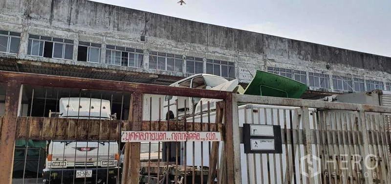 ที่ดิน ขายในLat Krabang, Bangkok - ประตูรั้วโลหะทางเข้า มีรถบรรทุกและอาคารโรงงานเก่าด้านหลัง