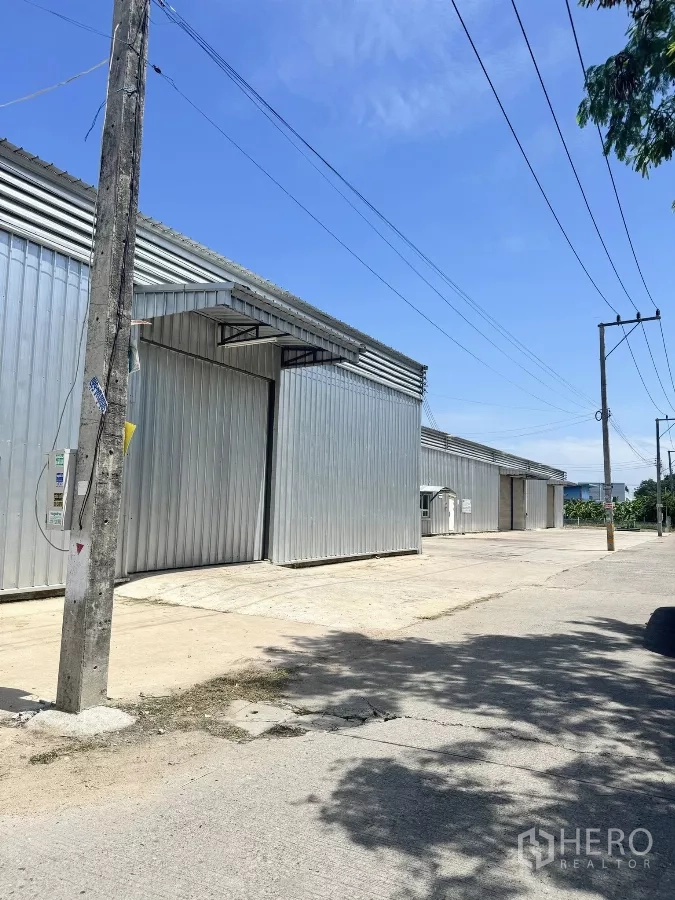 Warehouse for rent in Bang Lamung, Chon Buri - Row of adjoining metal warehouses along a quiet street with overhead power lines.