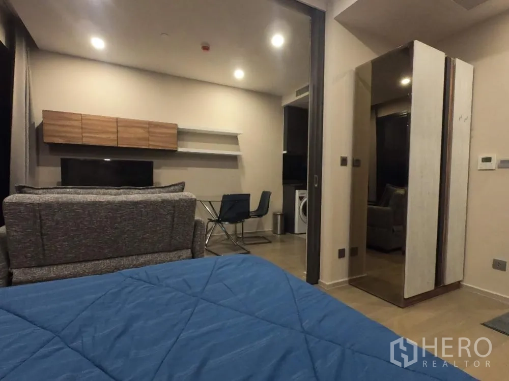 Condominium for rent in Watthana, Bangkok - Open-plan sleeping area facing a TV wall, sofa, and glass dining table near the kitchenette.