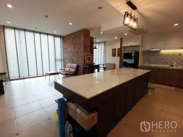 Condominium for rent or sale in Bang Rak, Bangkok - Spacious living and kitchen with long marble island, brick feature wall, and full-height blinds.