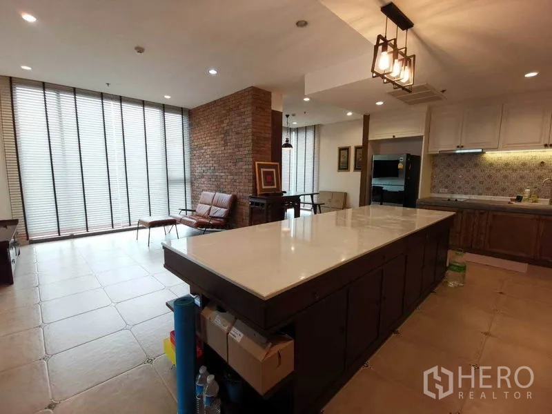 Condominium for rent or sale in Bang Rak, Bangkok - Spacious living and kitchen with long marble island, brick feature wall, and full-height blinds.