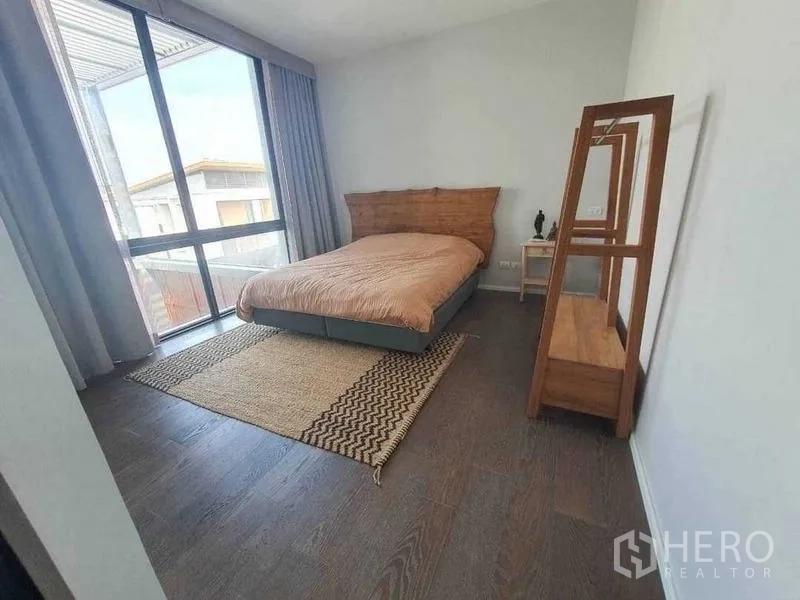 Detached House for rent or sale in Prawet, Bangkok - Bedroom with large window, wooden headboard and floor mirror.