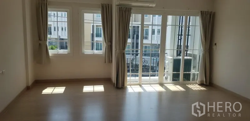 联排别墅 出租在Bang Na, Bangkok - 宽敞卧室，大窗与阳台门，配窗帘和空调。