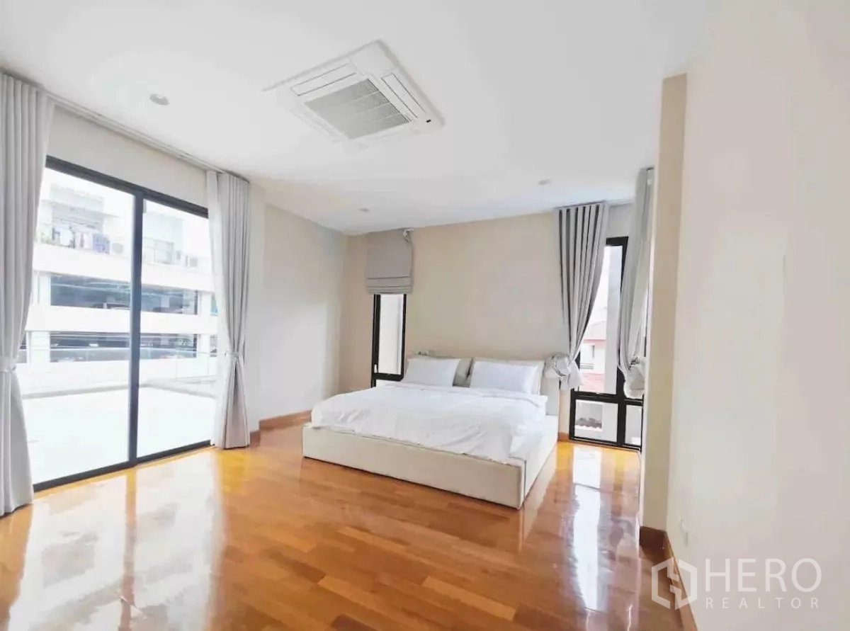 独立式住宅 出租在Phaya Thai, Bangkok - 转角卧室，亮面木地，环景窗与灰色窗帘。