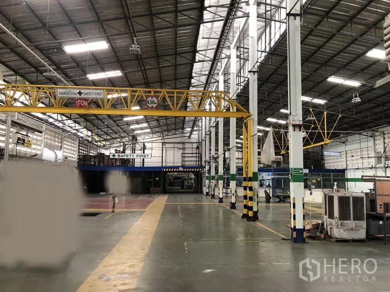 Factory for rent in Lam Luk Ka, Pathum Thani - Spacious factory floor with high steel roof, skylights, white columns and a yellow 1‑ton overhead crane, marked safety aisles visible.
