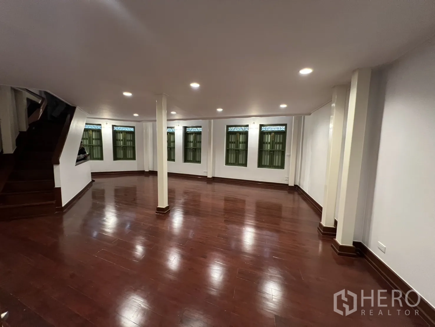 Shophouse for rent in Samphanthawong, Bangkok - Spacious upper floor with polished wooden flooring, recessed lighting, support columns, green-shutter windows and a staircase—ideal for office or showroom use.