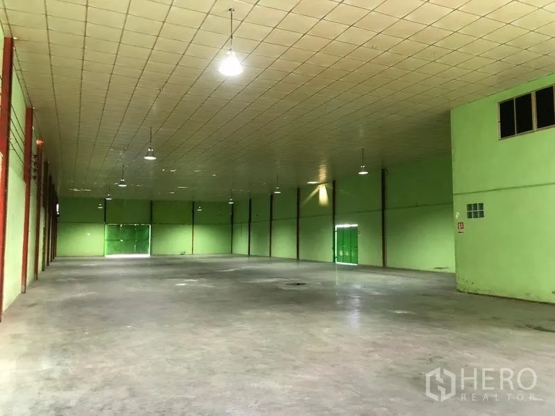 Factory for rent in Sam Khok, Pathum Thani - Large column-free storage space with hanging lights and a green roller door.