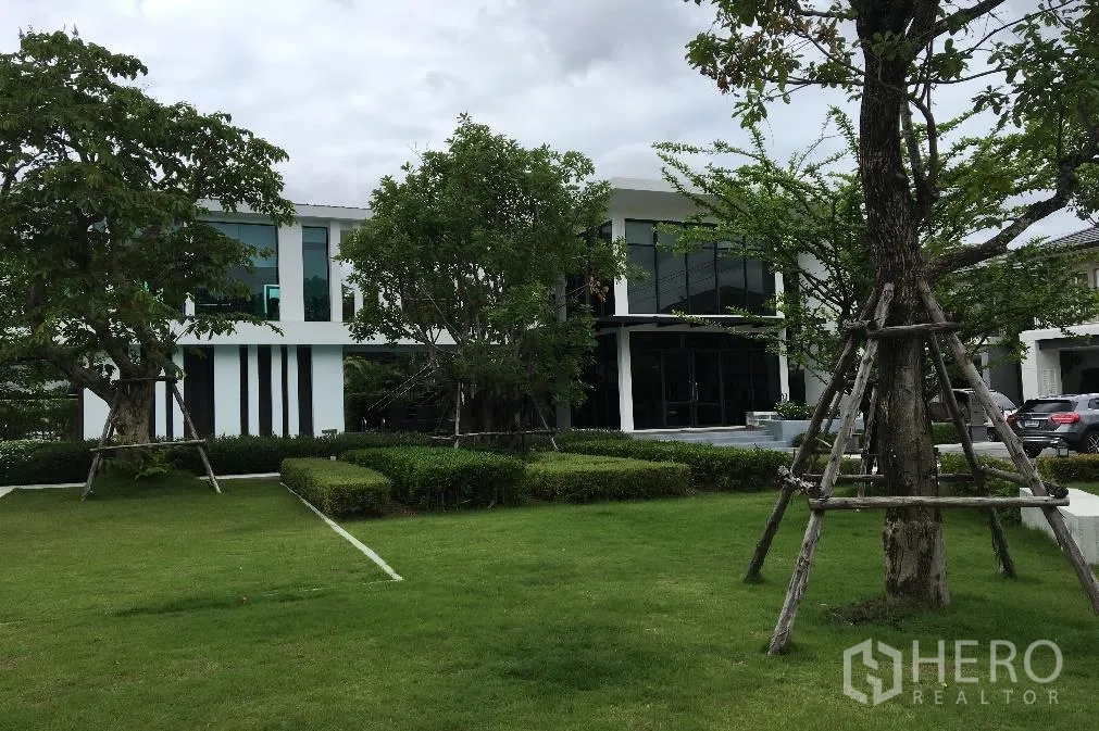 Detached House for rent or sale in Bang Na, Bangkok - Estate clubhouse with modern facade, large green lawn, hedges and mature trees.