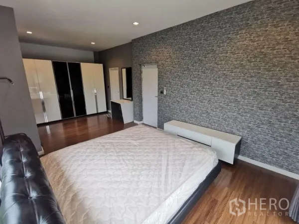 Detached House for rent in Prawet, Bangkok - Master bedroom view with textured feature wall, TV console, vanity and glossy wardrobes.
