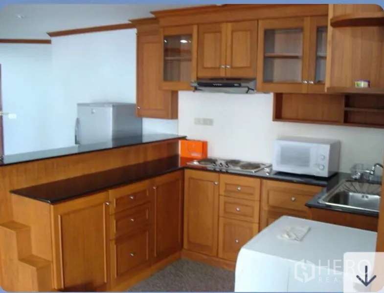 Condominium for rent in Ratchathewi, Bangkok - U-shaped kitchen with wooden cabinets, black countertops, cooktop and sink