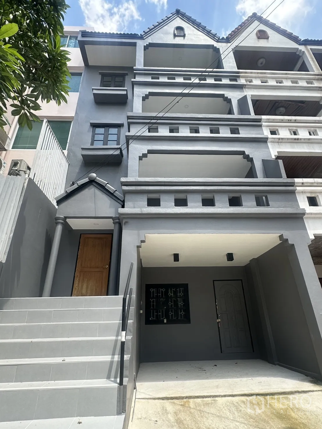 Townhouse for rent in Watthana, Bangkok - Four-storey grey townhouse exterior with multiple balconies, front steps, and a covered parking bay.