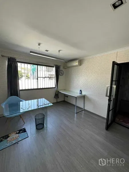 ทาวน์เฮาส์ ขายในLat Phrao, Bangkok - ห้องทำงานสว่างพร้อมโต๊ะกระจก หน้าต่างมีเหล็กดัด ผนังอิฐสีขาว และเครื่องปรับอากาศ