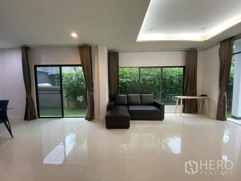 Detached House for rent in Bang Kapi, Bangkok - L-shaped sofa facing full-height windows and sliding doors opening to the lawn.