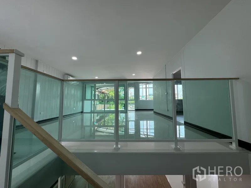 Townhouse for sale in Bueng Kum, Bangkok - Upper landing with glass balustrade overlooking a bright open space.