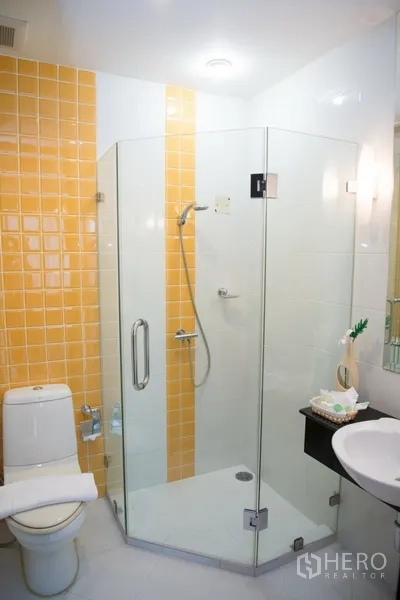 คอนโด ให้เช่าในKhlong Toei, Bangkok - ห้องน้ำสมัยใหม่ ตู้อาบน้ำกระจก โถสุขภัณฑ์ และอ่างล้างหน้า ผนังสีเหลือง