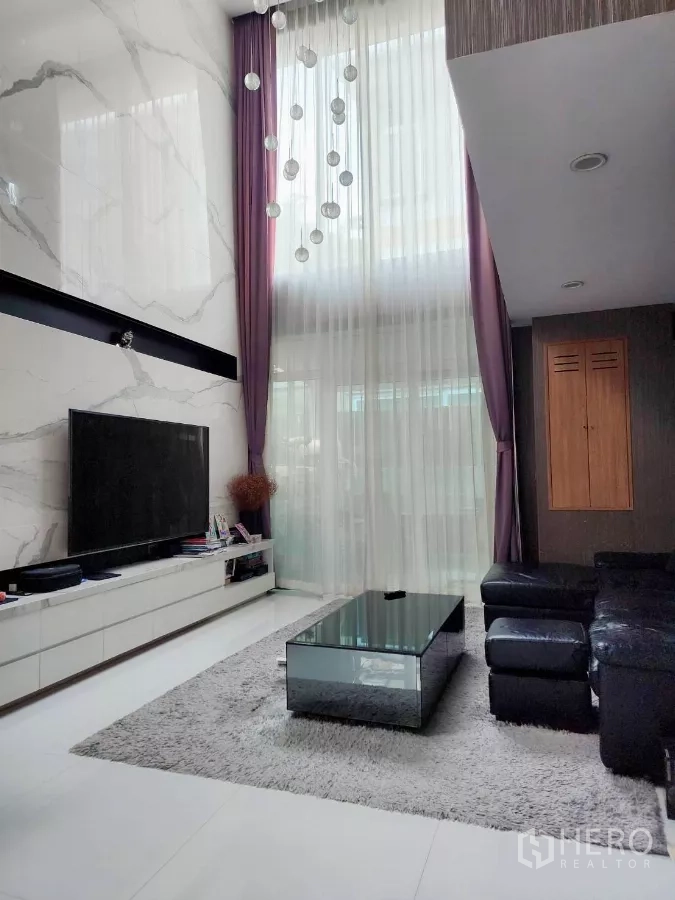 บ้าน ให้เช่าหรือขายในChatuchak, Bangkok - ห้องนั่งเล่นเพดานสูง ผนังหินลาย ทีวีจอใหญ่ และโซฟาหนัง