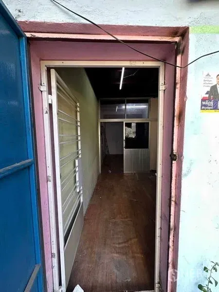 Shophouse for rent in Samphanthawong, Bangkok - Narrow entry corridor with wood-look flooring, a white security-grille window and fluorescent lighting leading into the shophouse.