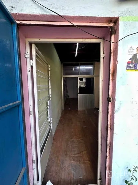 Shophouse for rent in Samphanthawong, Bangkok - Narrow entry corridor with wood-look flooring, a white security-grille window and fluorescent lighting leading into the shophouse.