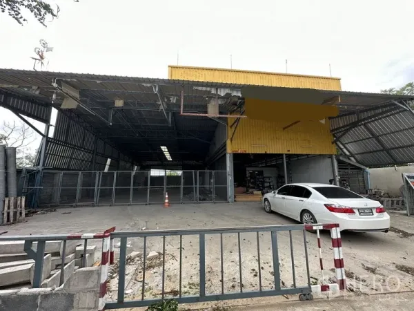 Warehouse for sale in Bang Khen, Bangkok - Front view of Bang Khen warehouse with wide covered loading bay, yellow facade, gated entrance and parking area.