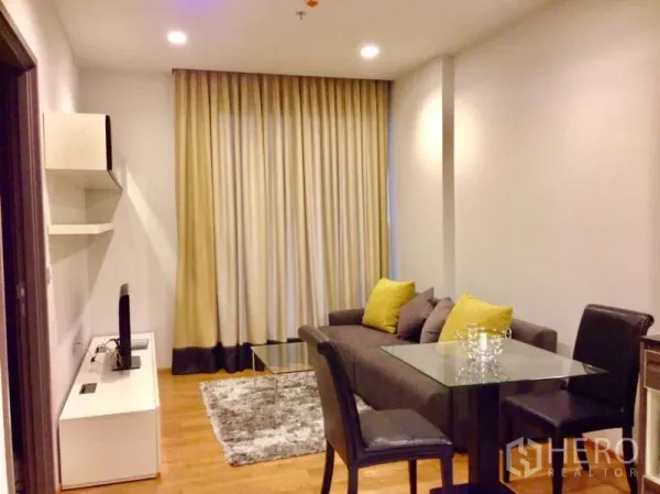 คอนโด ให้เช่าในKhlong Toei, Bangkok - ห้องนั่งเล่นพร้อมโซฟาโต๊ะกระจก ชั้นวางทีวี และผ้าม่านสูงจรดเพดาน