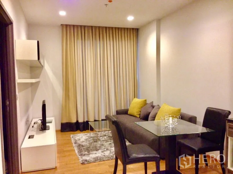 คอนโด ให้เช่าในKhlong Toei, Bangkok - ห้องนั่งเล่นพร้อมโซฟาโต๊ะกระจก ชั้นวางทีวี และผ้าม่านสูงจรดเพดาน