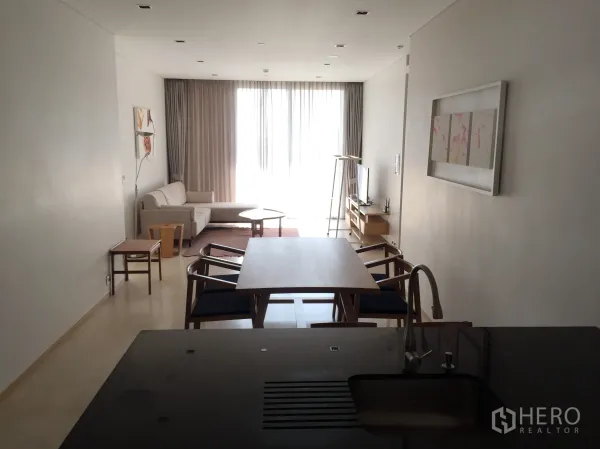 Condominium for rent in Bang Rak, Bangkok - Open-plan living and dining area with kitchen island, sofa, TV console and floor-to-ceiling sheer curtains.