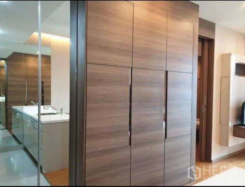 Condominium for rent in Bang Rak, Bangkok - Hallway featuring large built-in wooden wardrobes and a mirrored vanity leading to the bathroom.