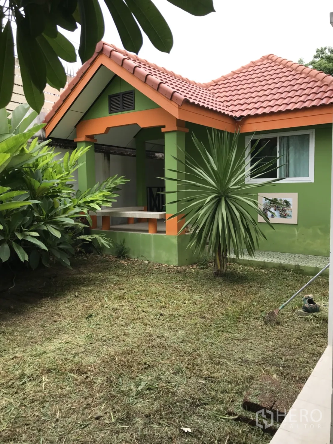 บ้าน ให้เช่าในLat Krabang, Bangkok - ภายนอกบ้านเดี่ยว โทนสีเขียวส้ม หลังคากระเบื้องสีอิฐ พร้อมสนามหญ้าและไม้ใบเขตร้อน